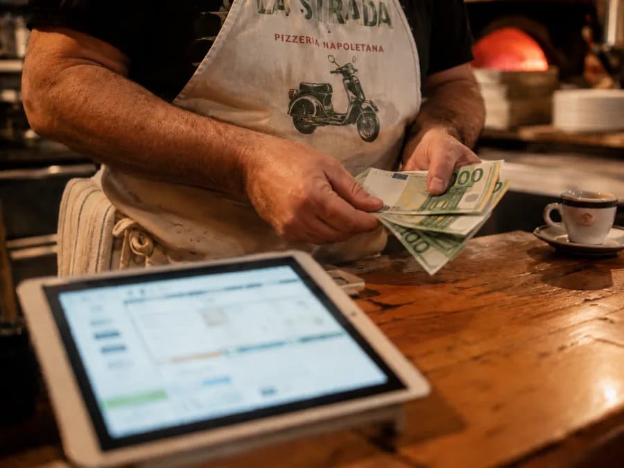 Pizzaiolo zaehlt Euro-Scheine an der Theke, iPad mit Bestellsystem im Vordergrund