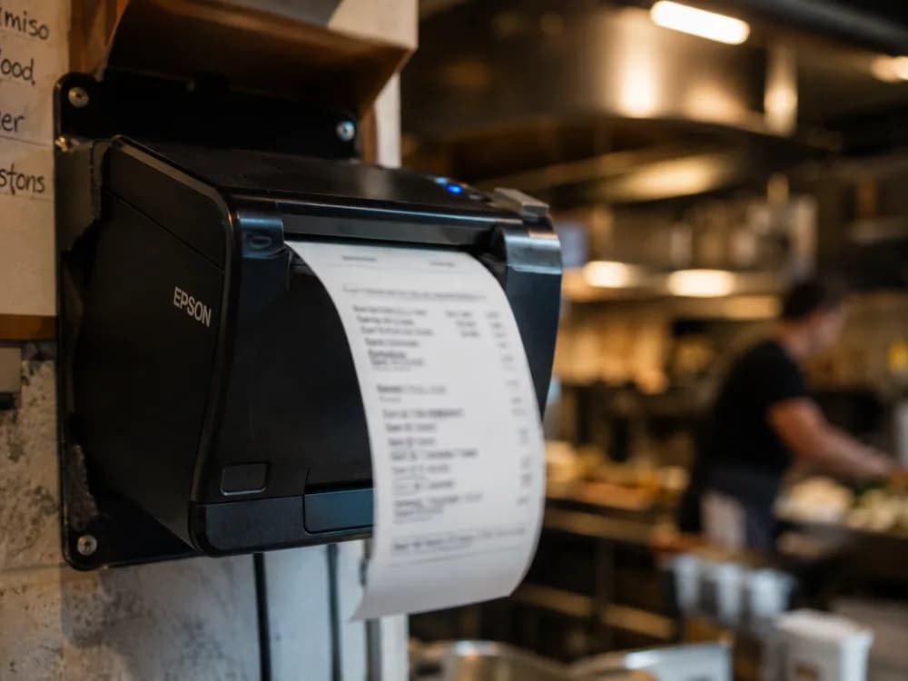 Epson-Bondrucker druckt frischen Bon, warme Kueche im Hintergrund